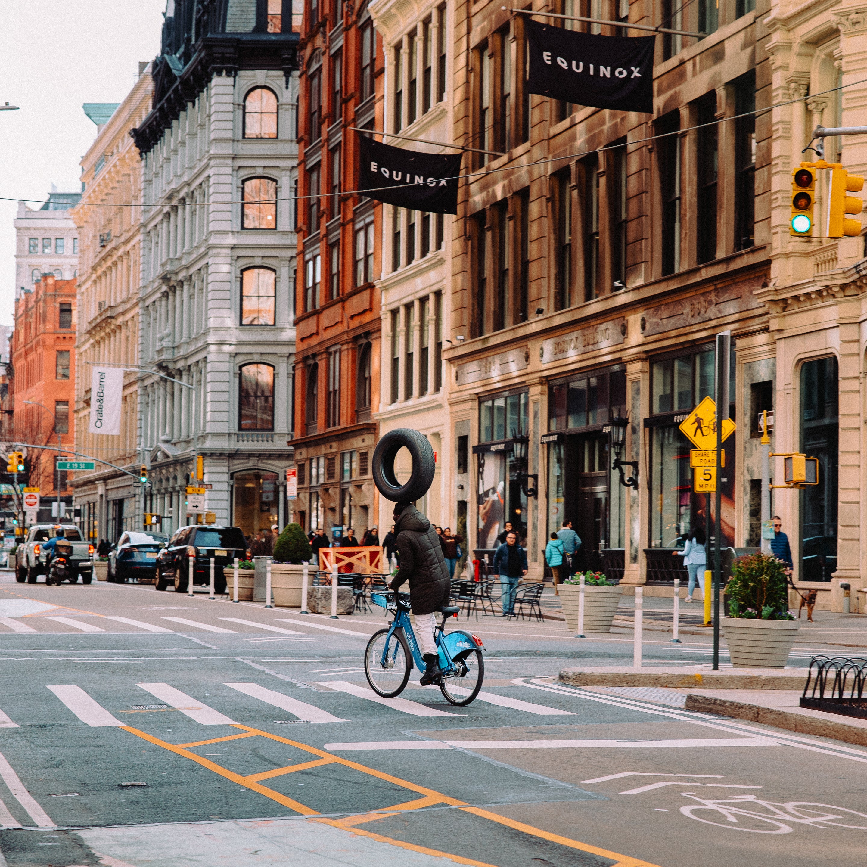 A photo print depicting a street scene in NYC with a skateboarder, buildings, and a cyclist on the road.