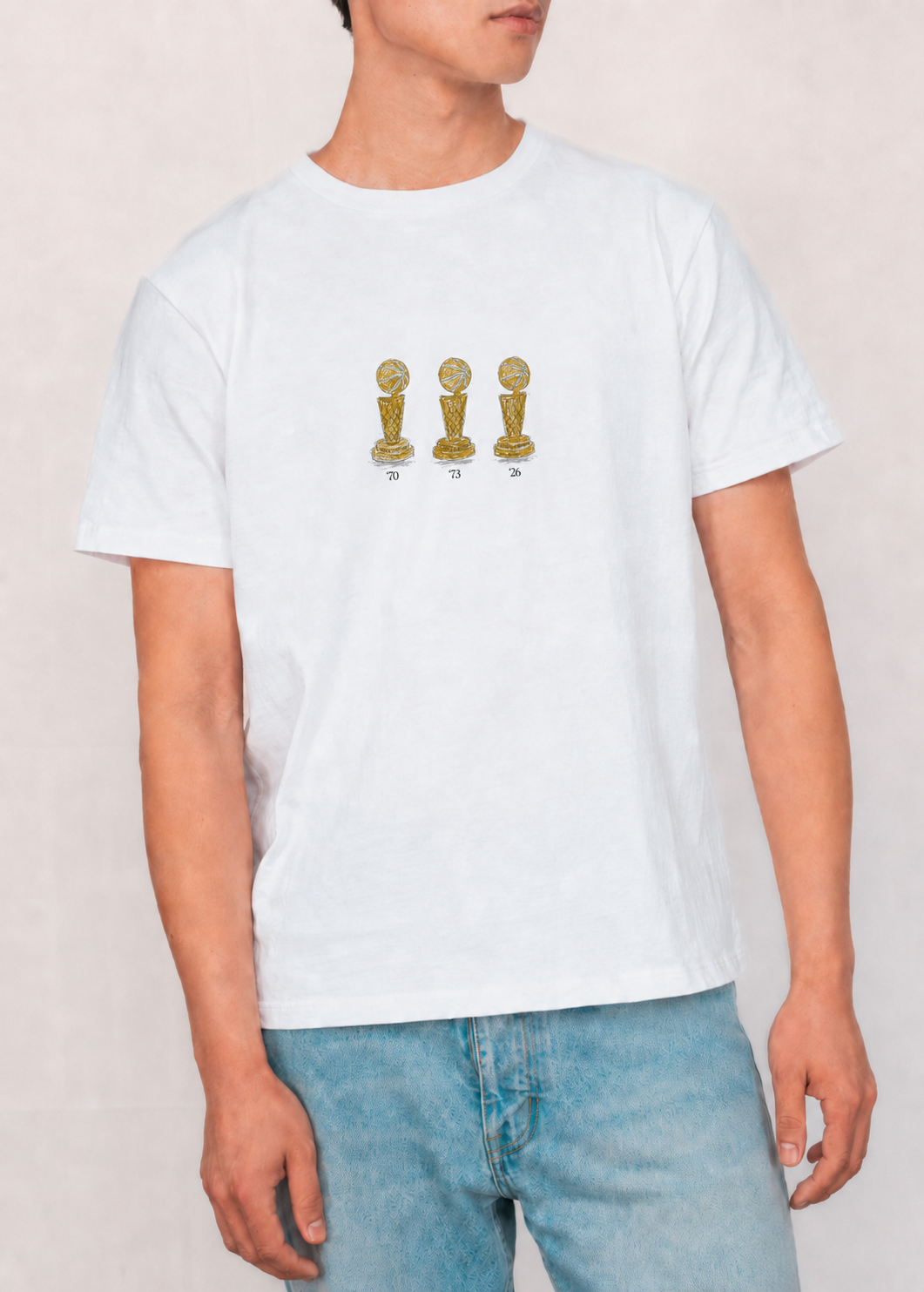Person wearing a white t-shirt with gold graphic design of trophies on a plain background